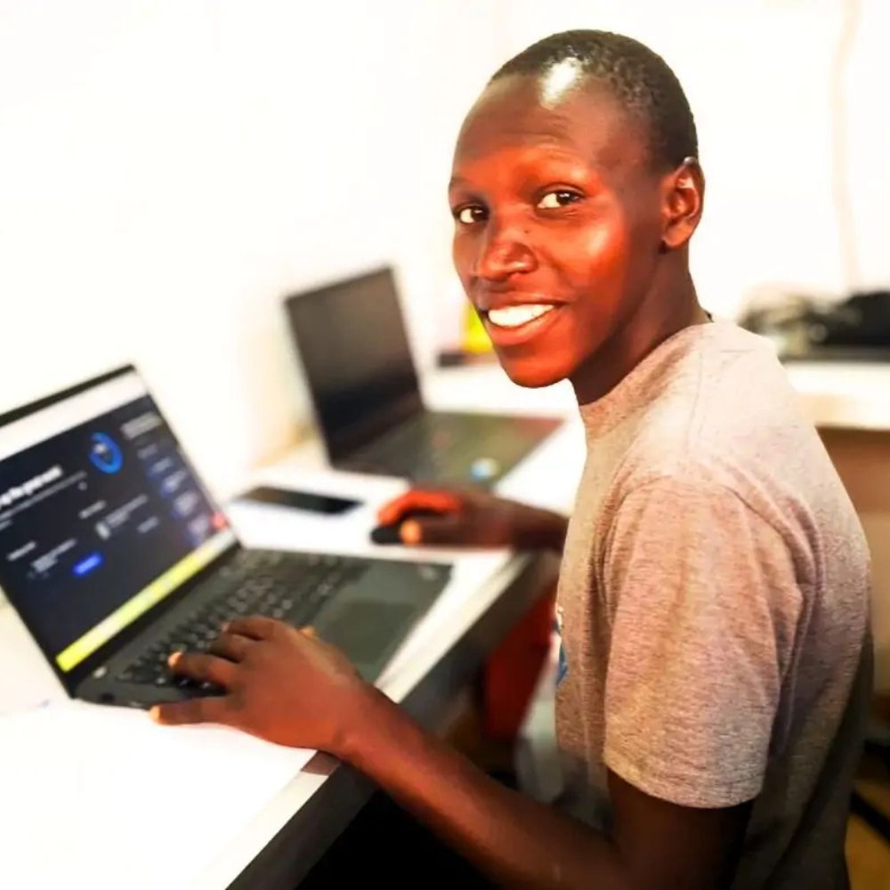 Smiling man seated at a desk, typing on a laptop and looking at the camera